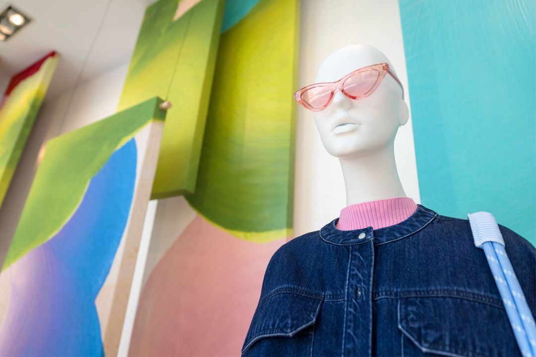 Spring Awakening window display: a mannequin in pink sunglasses and a denim jacket against hanging painted panels