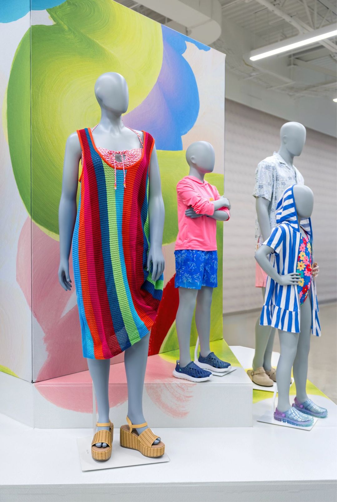 Spring Awakening display: a striped knit dress and kids' swim looks in front of a painted canvas